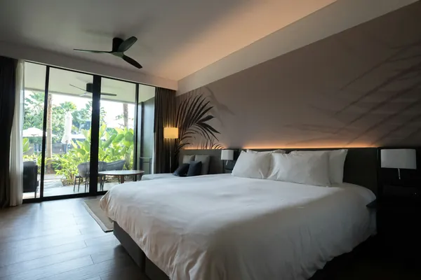 A hotel room with a king bed and glass doors to a garden